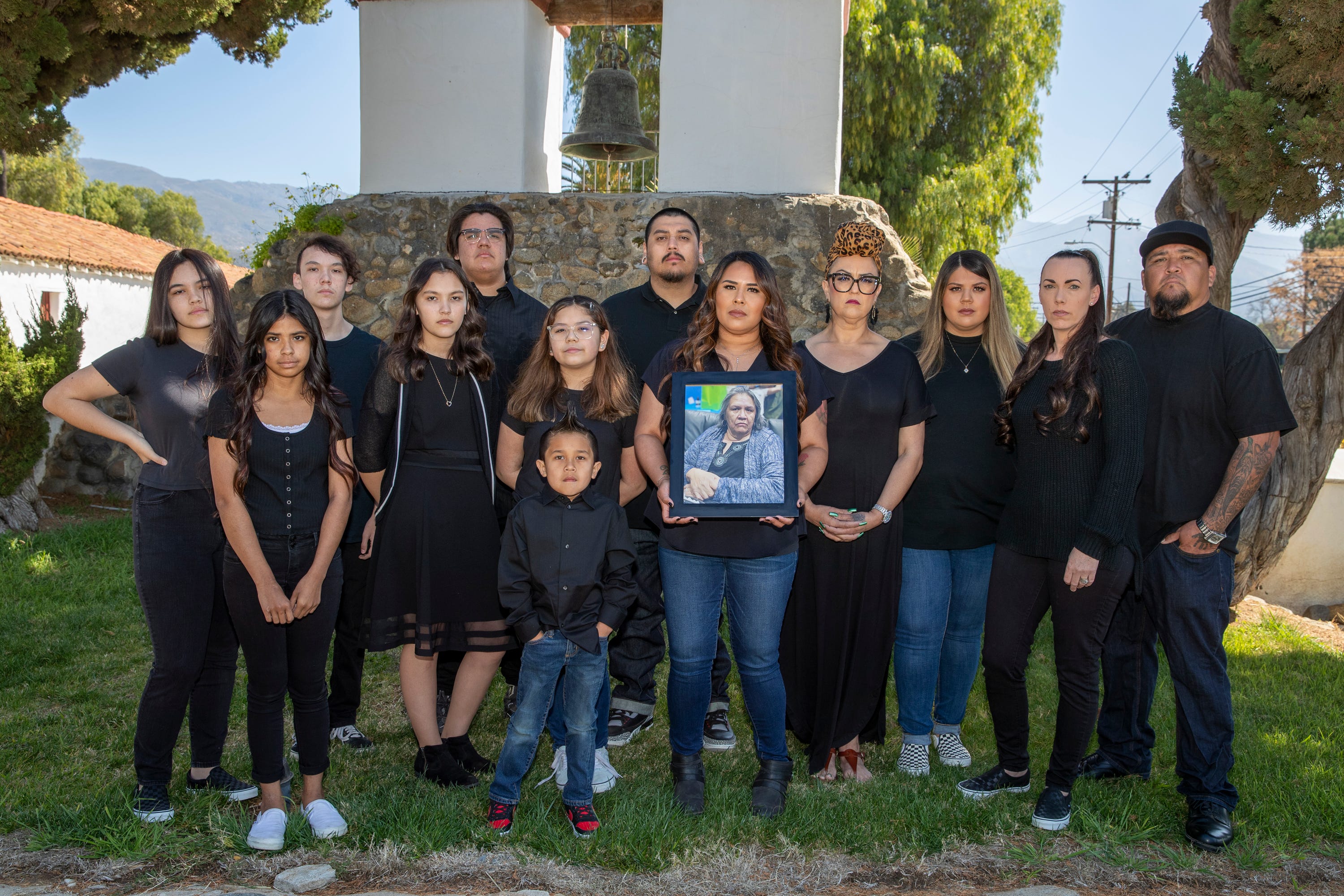 April Cantu, center, holds a photo of her late mother, Jo Ann Smith, who was flanked by a family outside of the San Antonio De Pala Mission in Pala, California on March 6, 2021.  Smith, a member of the Pala Band of Mission Indians died of COVID-19. 
