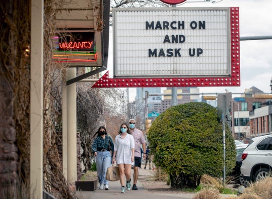 Juan Tenorio and his daughters, Abagail, 20, and Isabel, 18, walk past a sign encouraging masking in Austin on Tuesday, a day before the end of a statewide mask mandate.