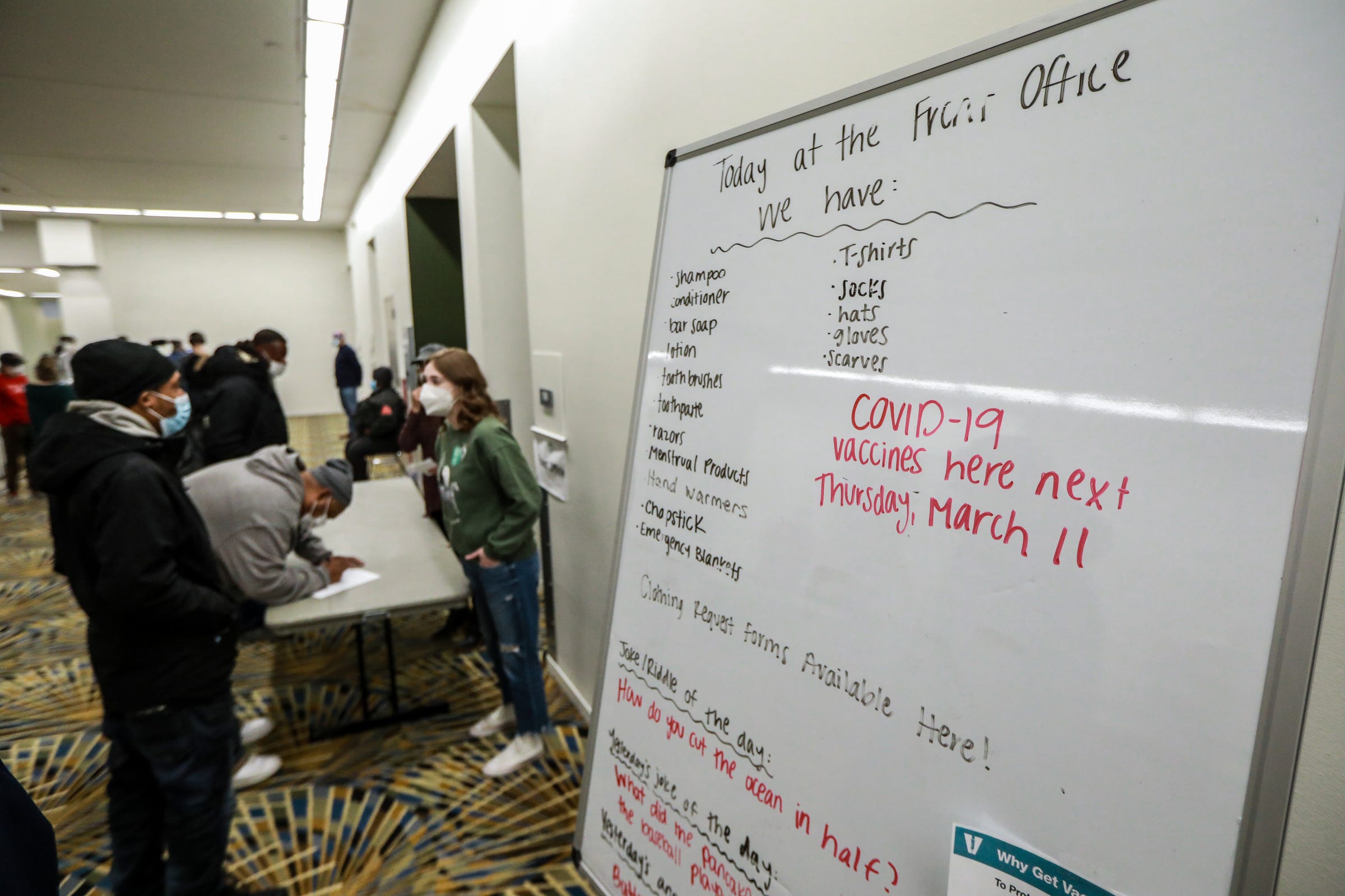 Men and women stop at the Front Office to receive vital resources like socks, gloves, and toiletries at the Pope Francis Center in TCF Center in downtown Detroit on March 6, 2021. The whiteboard also says COVID-19 vaccines will be available next Thursday, March 11th.