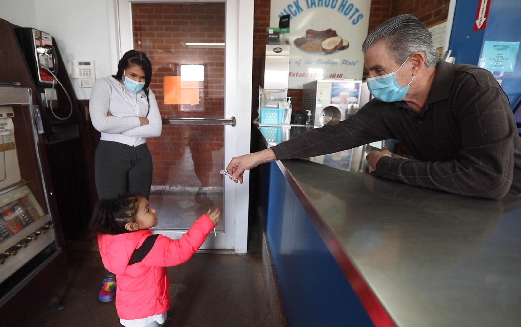 Alex Tahou, owner of Nick Tahou Hots, keeps lollipops on hand for little children. Here, he hands one to Amiyah Peters as her mom, Alexis Reed of Rochester, tells Tahou that the free lollipops are what her daughter remembers most about the restaurant.