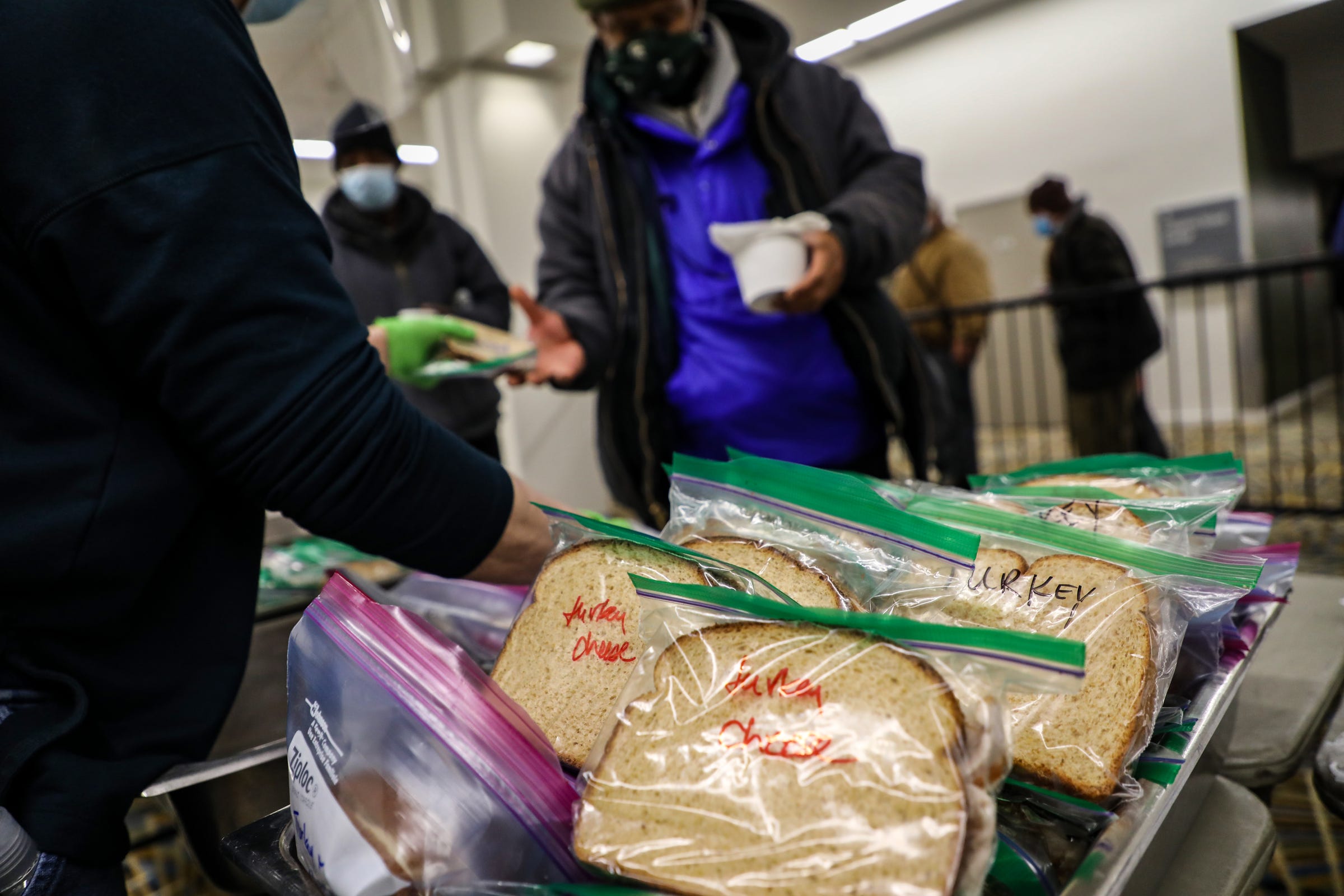 People wait in line behind a barrier to receive one of the two meals served by the Pope Francis Center temporarily relocated at the TCF Center in downtown Detroit to better accommodate the homeless population it serves during the coronavirus pandemic on Dec. 8, 2020.