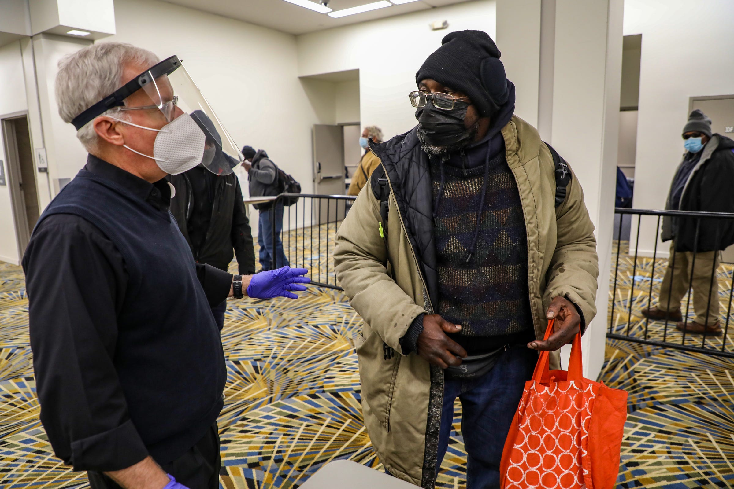 Father Tim McCabe, S.J. talks with Wayne Shropshire as he steps to the front of the line to receive one of the two free meals served by the Pope Francis Center temporarily relocated at the TCF Center in downtown Detroit to better accommodate the homeless population it serves during the coronavirus pandemic on Dec. 8, 2020.