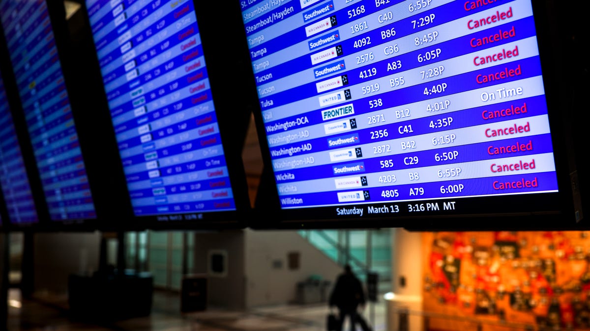 A man walks past a display board showing mostly canceled flights at Denver International Airport on March 13, 2021.
