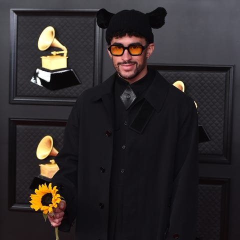 Bad Bunny holds a sunflower on the carpet.
