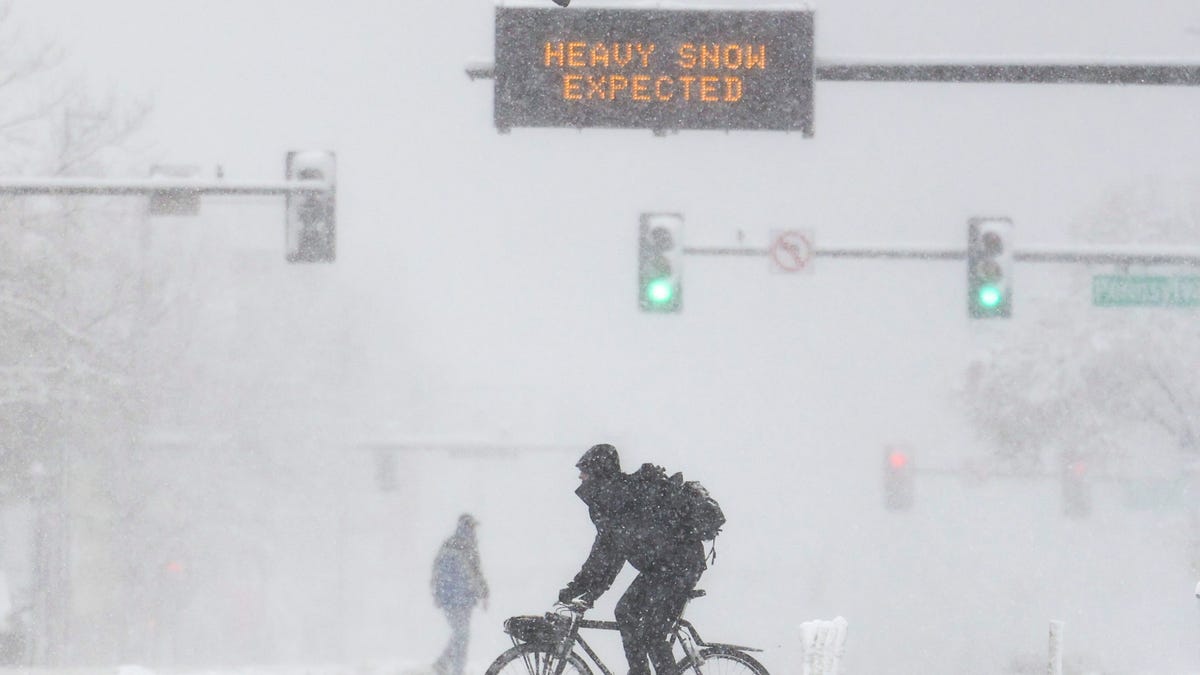 People cross Colfax Avenue as a sign warns of heavy snow on March 14, 2021 in Denver, Colo. 