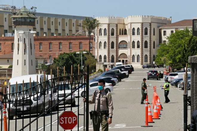 FILE - In this July 9, 2020, file photo, a correctional officer closes the main gate at San Quentin State Prison in San Quentin, Calif. The family of a 61-year-old California inmate who died of the coronavirus sued state corrections officials Tuesday, March 16, 2021, blaming a botched transfer of infected inmates to San Quentin State Prison that killed 28 inmates and a correctional officer in 2020. (AP Photo/Eric Risberg, File)