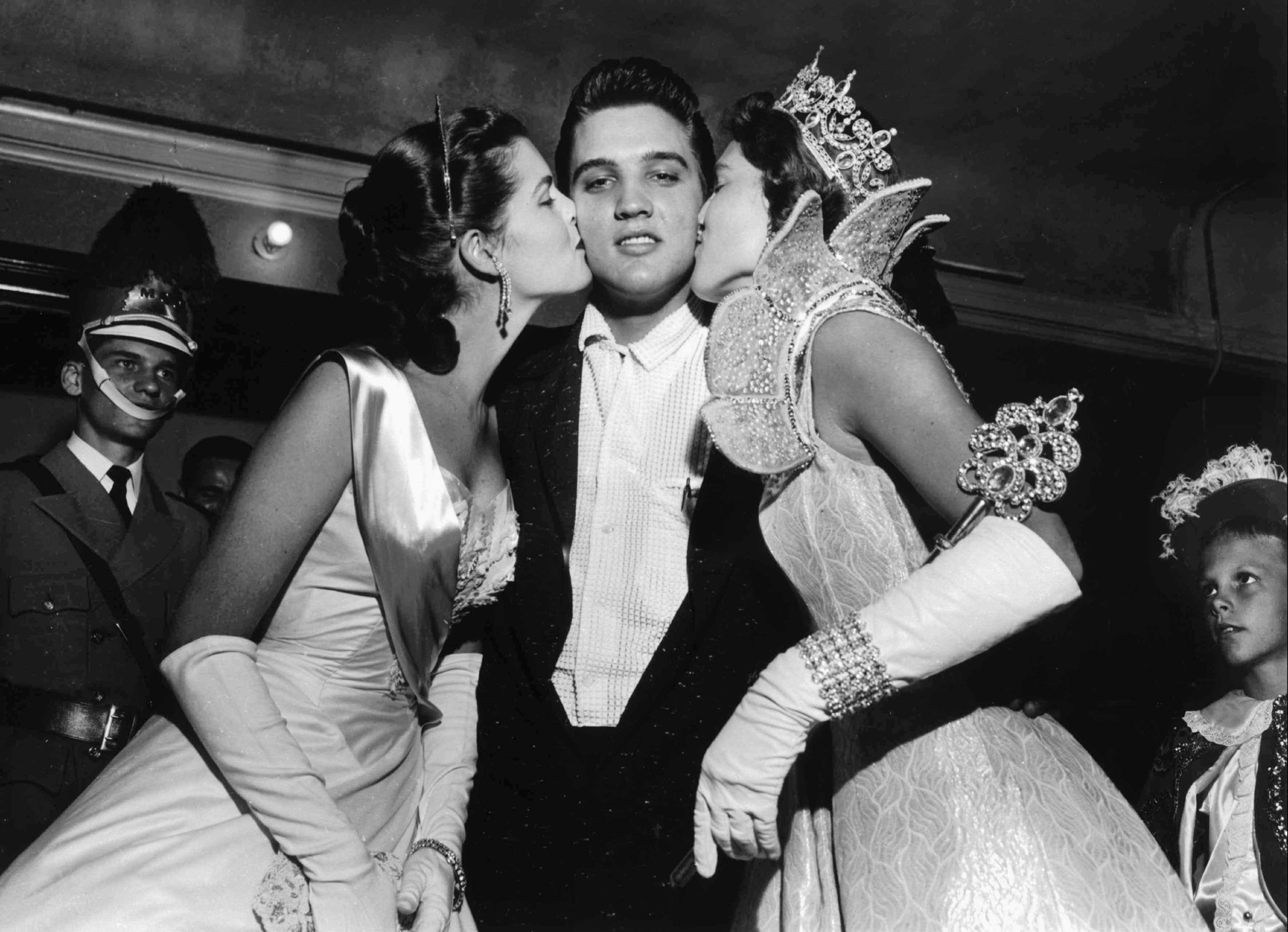 Elvis Presley is kissed on the cheek by Maid of Cotton Patricia Cowden and Memphis Cotton Carnival Queen Clare Mallory just before the rock ‘n’ roll singer walked on stage before a packed Ellis Auditorium audience on May 15, 1956.