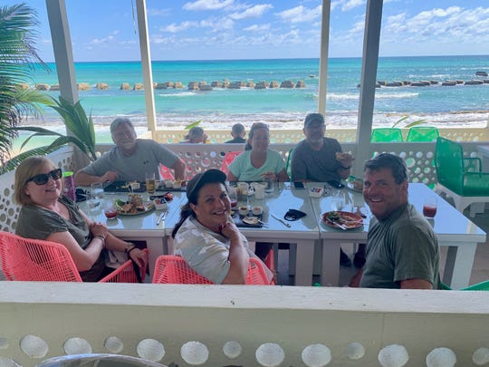 Lucia Rooney, in a light green shirt facing the camera, dines with friends and family members in Riviera Maya, Mexico.