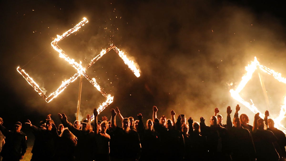 Members  of the National Socialist Movement, one of the largest neo-Nazi groups in the U.S., hold a swastika burning after a 2018 rally in Georgia.