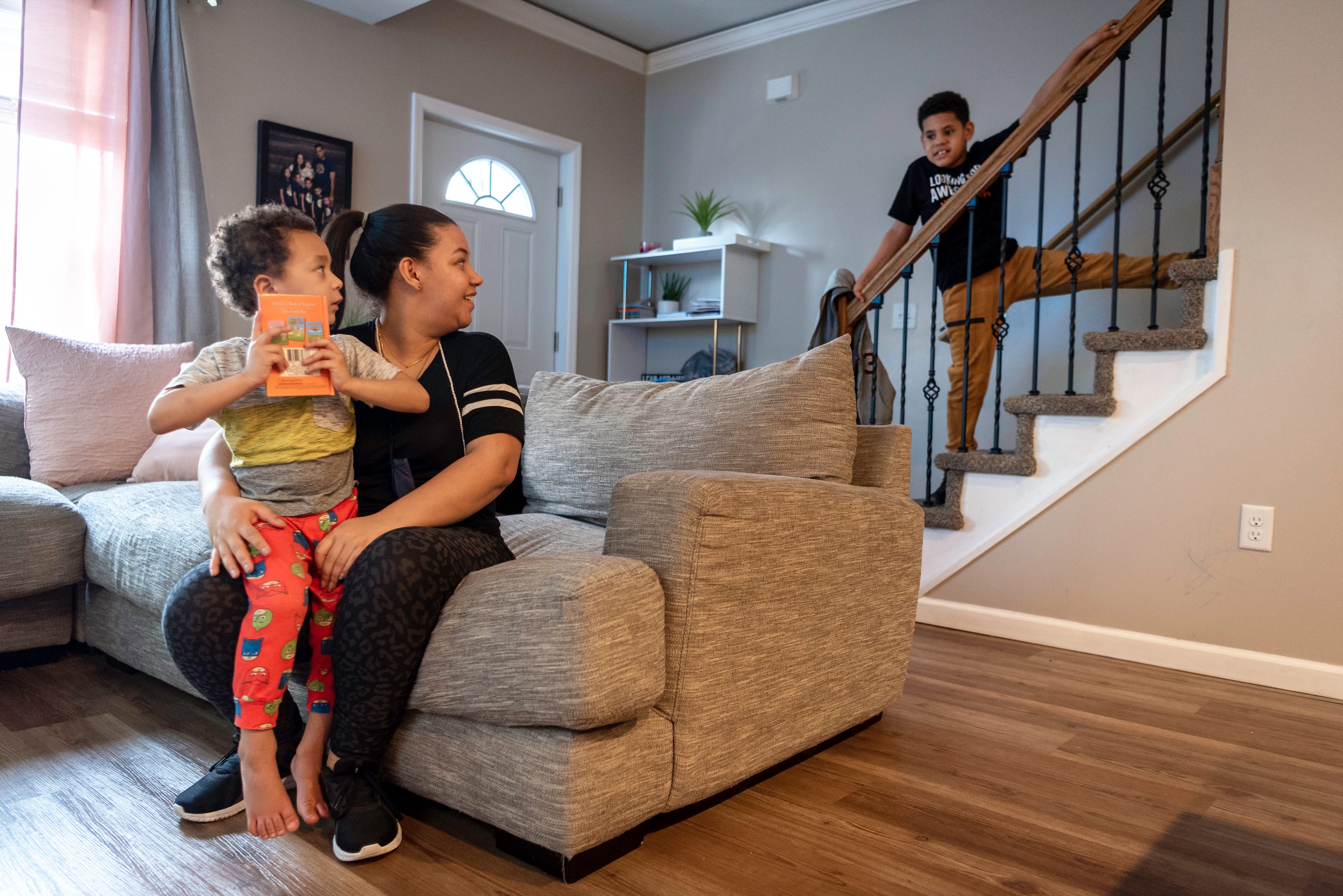 Raylin De La Cruz, 10 emerges from upstairs after changing his clothes while Dafani Peralta reads a book with her youngest son, David De La Cruz, 3.