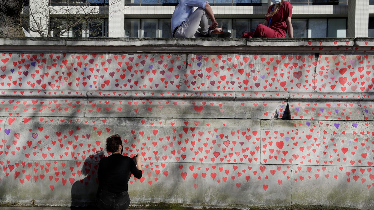 Hospital staff from St Thomas' Hospital watch from the top of the wall as members of bereaved families paint red hearts on the COVID-19 Memorial Wall opposite the Houses of Parliament on the Embankment in London, Monday March 29, 2021.