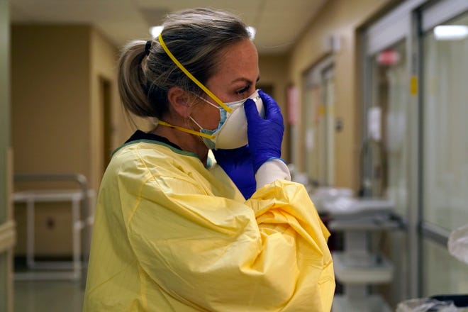 In this Nov. 24, 2020, file photo, registered nurse Chrissie Burkhiser puts on personal protective equipment as she prepares to treat a COVID-19 patient in the in the emergency room at Scotland County Hospital in Memphis, Mo. (AP Photo/Jeff Roberson, File)