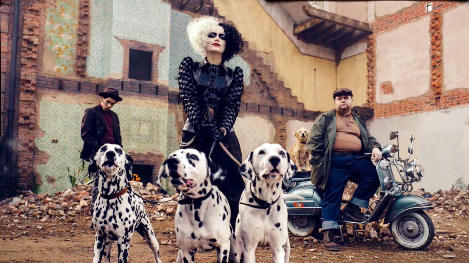 Cruella Deville and two men outside of a beaten-down building. Cruella is holding three dalmatians on a leash. One of the men is on a vintage Vespa.