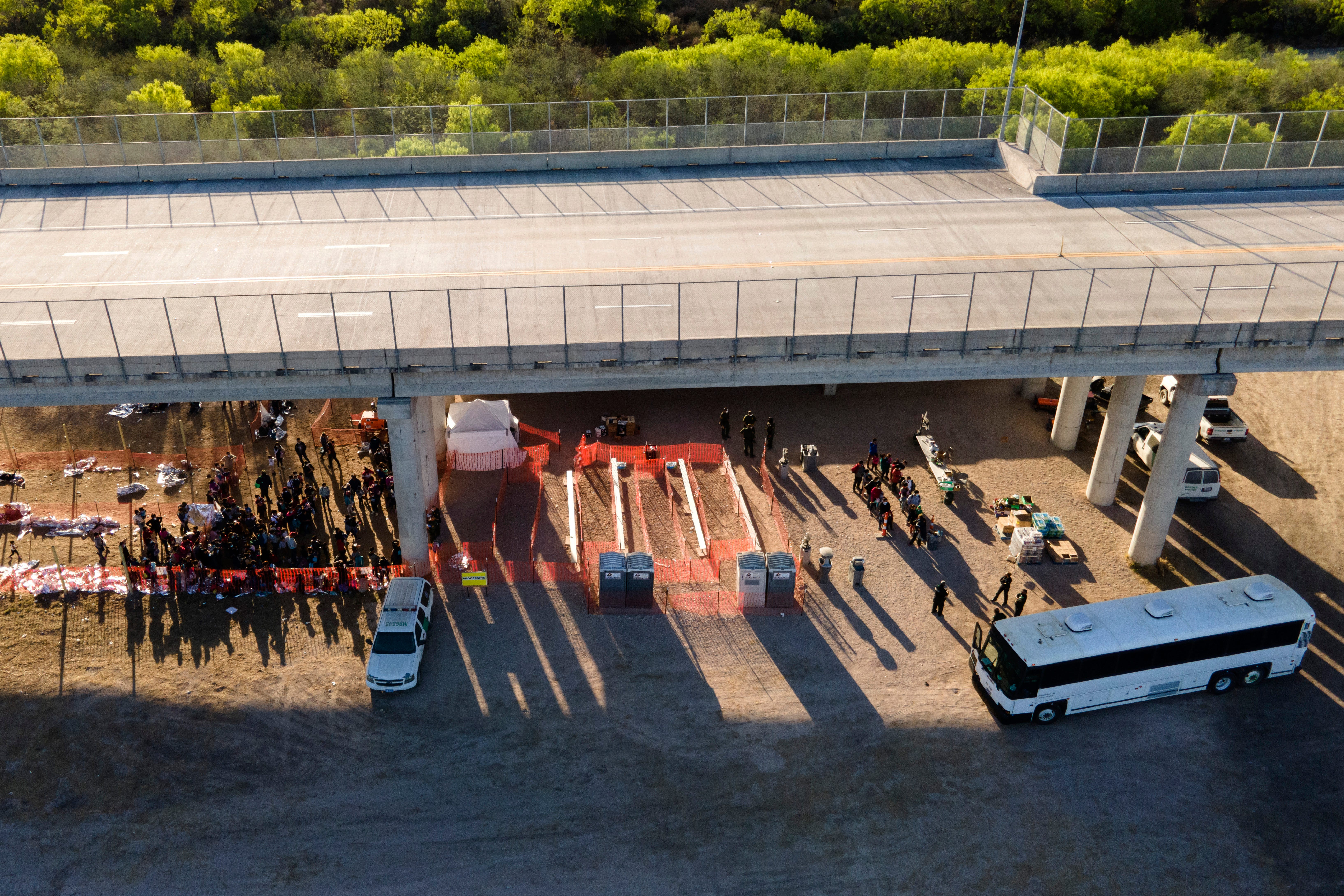 In this photo taken by a drone, migrants are seen in custody at a U.S. Customs and Border Protection processing area under the Anzalduas International Bridge, Thursday, March 18, 2021, in Mission, Texas. A surge of migrants on the Southwest border has the Biden administration on the defensive. The head of Homeland Security acknowledged the severity of the problem Tuesday but insisted it's under control and said he won't revive a Trump-era practice of immediately expelling teens and children. (AP Photo/Julio Cortez)