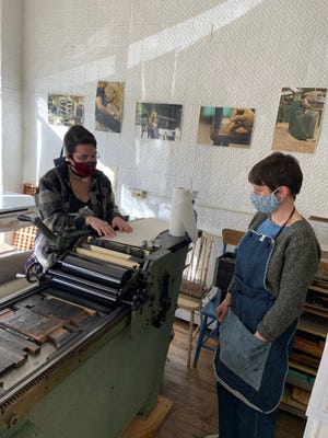 Volunteer Heidi Hosmer, left, gives the Chair City Community Workshop letterpress one final spin as Director Tracie Pouliot looks on. The Community Workshop closed the doors to its Central Street headquarters on March 29.