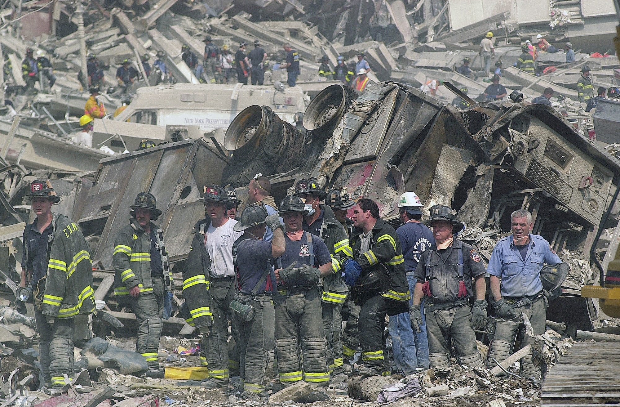 New York City firefighters take a break near a demolished ladder truck in the remains of the World Trade Center on Sept. 12, 2001.