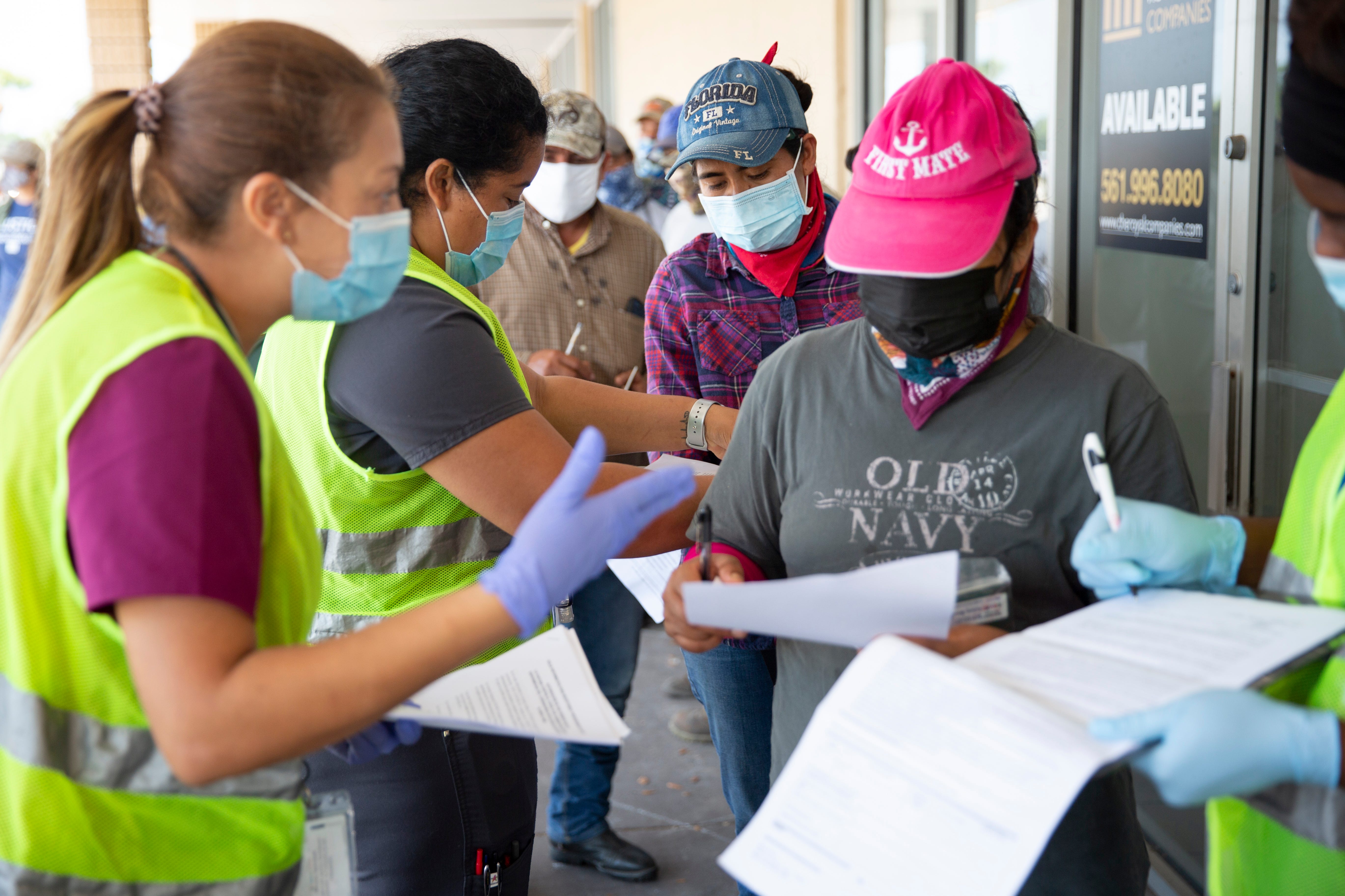 Healthcare Network employees help farmworkers fill out their paperwork as they wait in line during a vaccine clinic for farmworkers at the Florida Department of Health in Collier County site on Lake Trafford Road in Immokalee on Saturday, April 10, 2021.