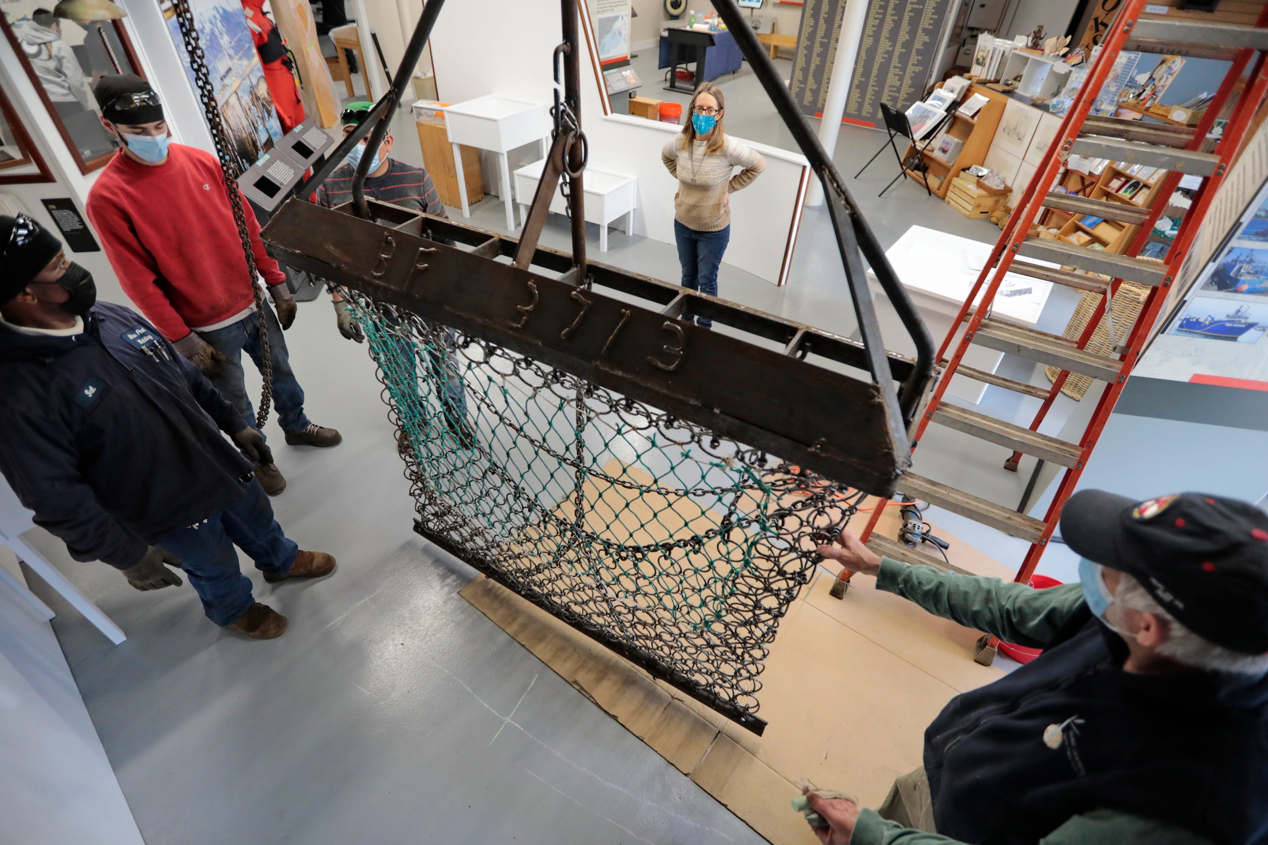 Laura Orleans, director, looks on, as a new one-third scale scallop dredge manufactured by Blue Fleet Welding Services is installed at the New Bedford Fishing Heritage Center.