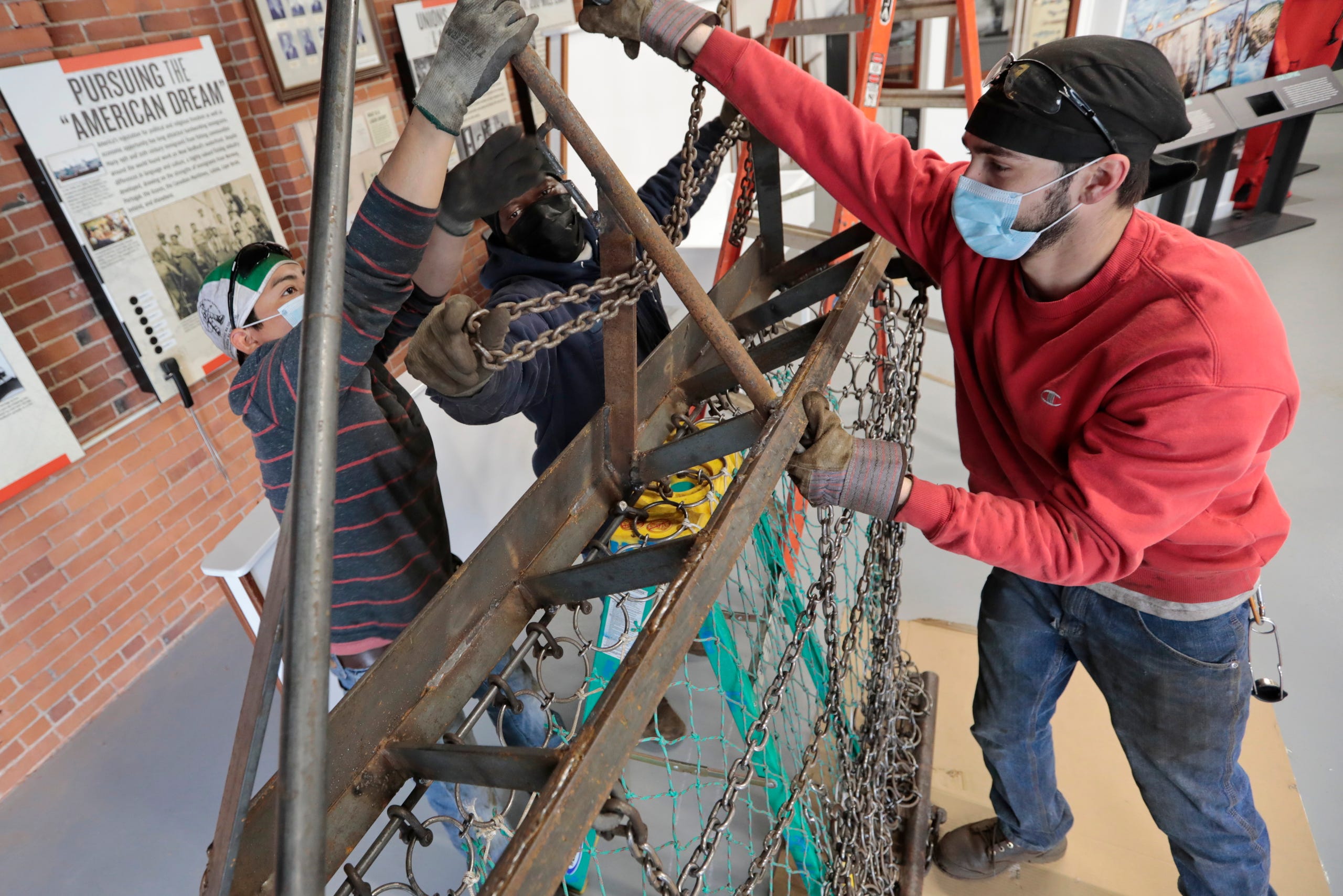 Blue Fleet Welding Services welders, Domingo Ixcuna Lucas, Sal Sequeira and Dave St Pierre, install the one-third scallop dredge they manufactured for the newly redone interior of the New Bedford Fishing Heritage Center.