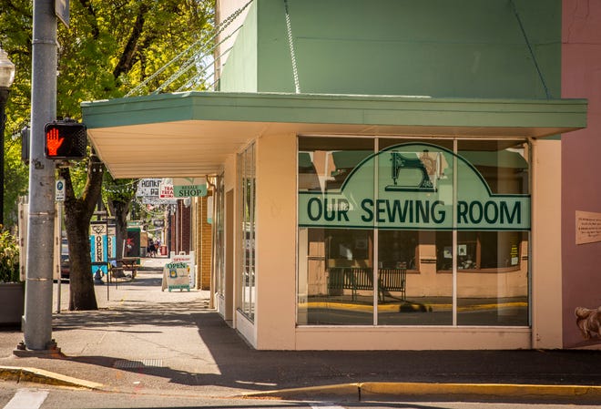 Our Sewing Room, now permanently closed, sits empty on Main Street in Springfield as so many businesses have been similarly impacted by the pandemic. Open signs and restaurant patrons are seen just further down the sidewalk.