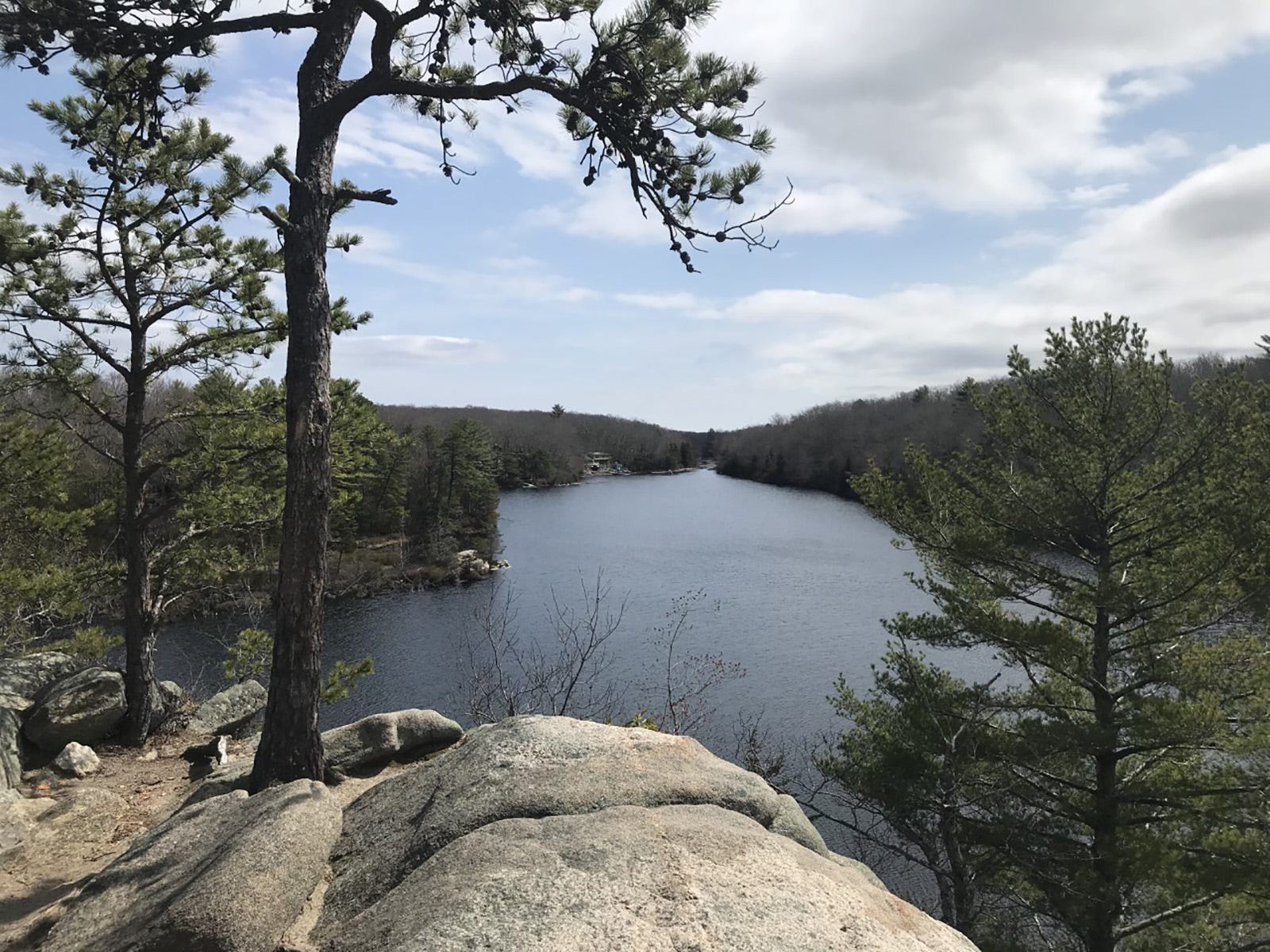 From a rocky outcropping a large tree-lined pond can be seen.