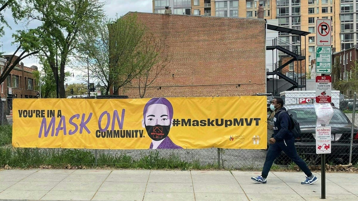 A person wearing a mask walks by a banner encouraging the use of face coverings in Washington, DC on April 16, 2021.