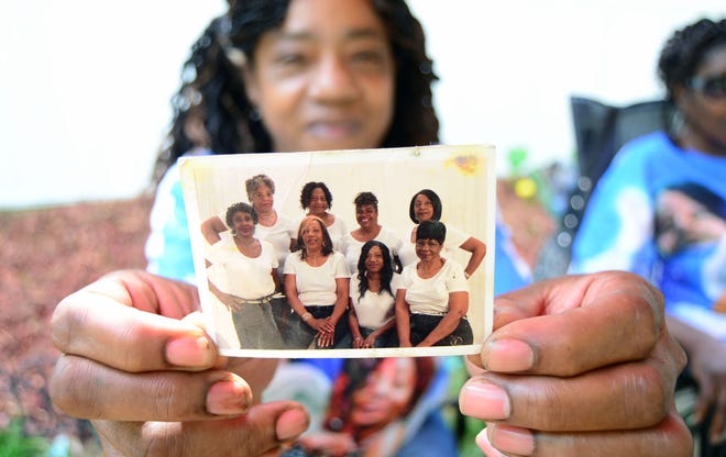 Ella Chism holds a photo of her sisters. Sandra Lockett Huckleberry is seen in the back row on the right end.