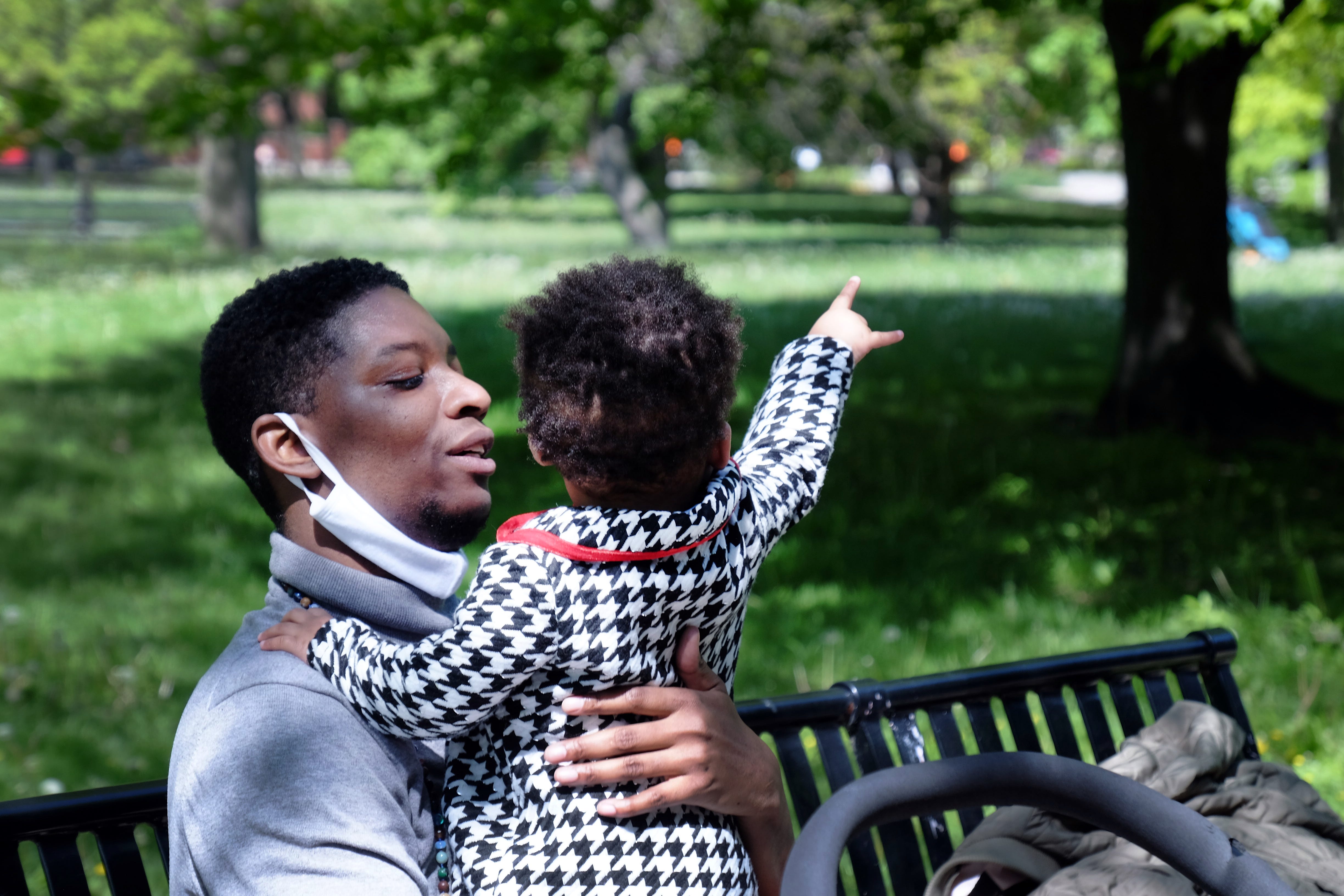 Myles Brady-Davis and their daughter, Zayn, sit by the Model Yacht Basin in Harold Washington Park in Hyde Park, Chicago on May 14, 2021.