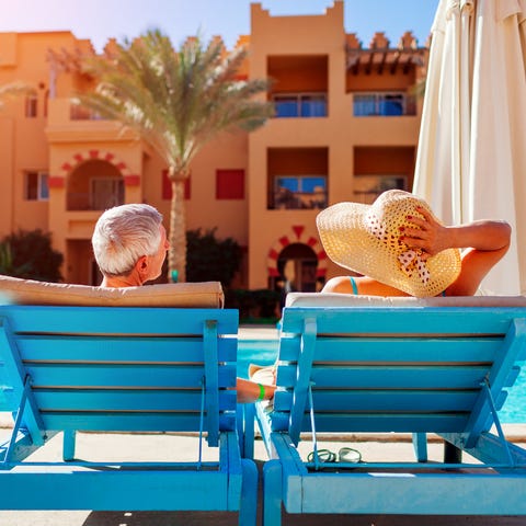 A senior couple relax by a swimming pool lying on 