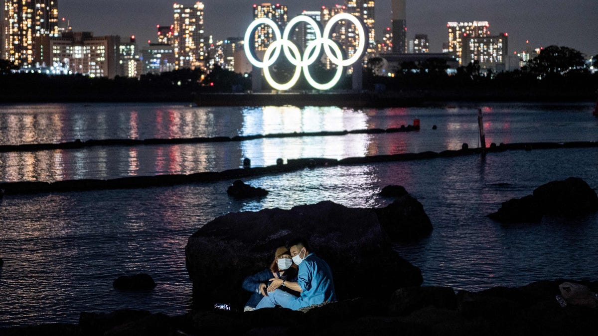 A couple poses for pictures before the lit Olympic rings at the Odaiba waterfront in Tokyo.