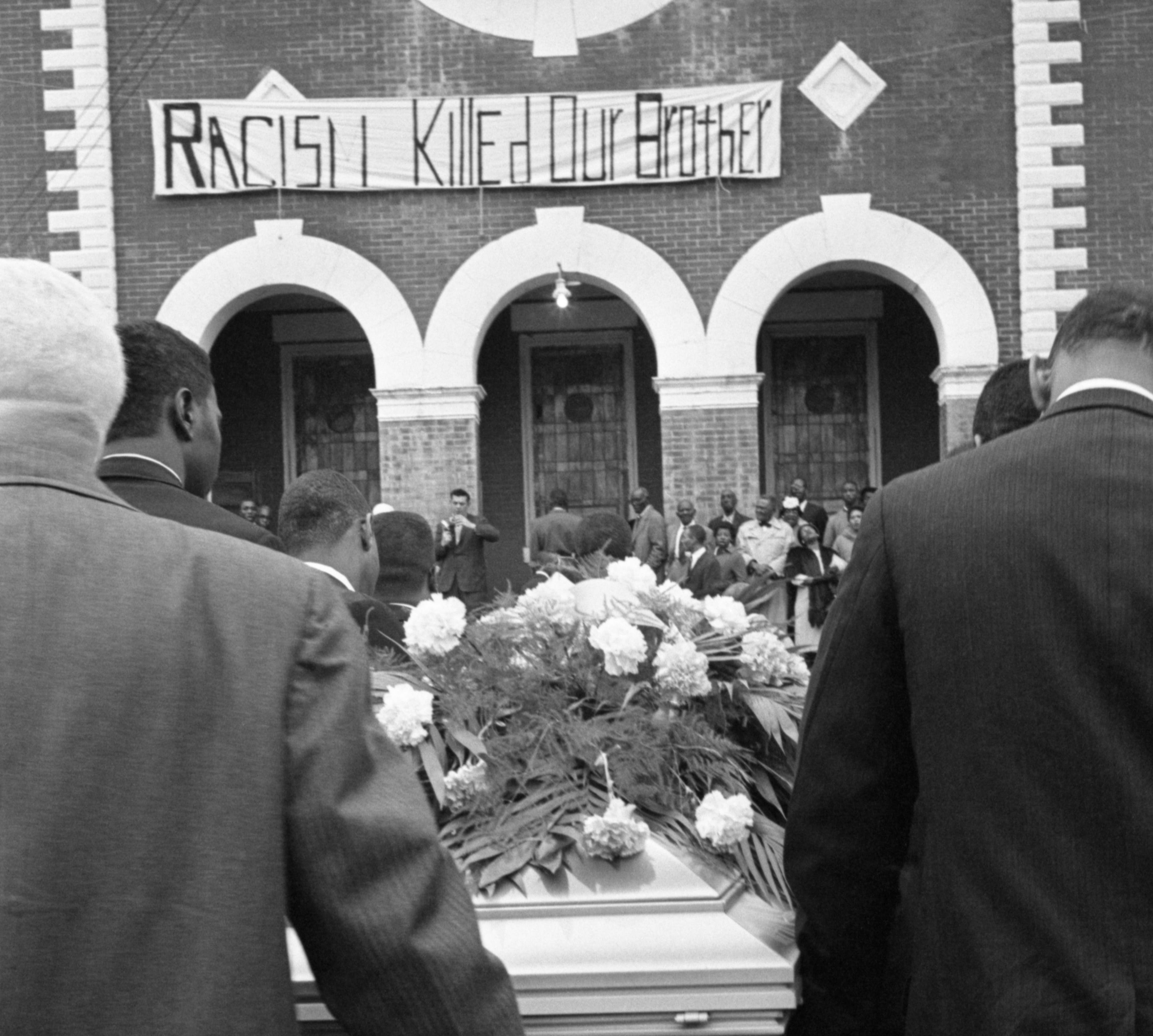 The casket bearing the body of Jimmie Lee Jackson is carried into a church in Selma, Alabama for funeral services on March 3, 1965. A sign in front of the church reads, "Racism Killed Our Brother."