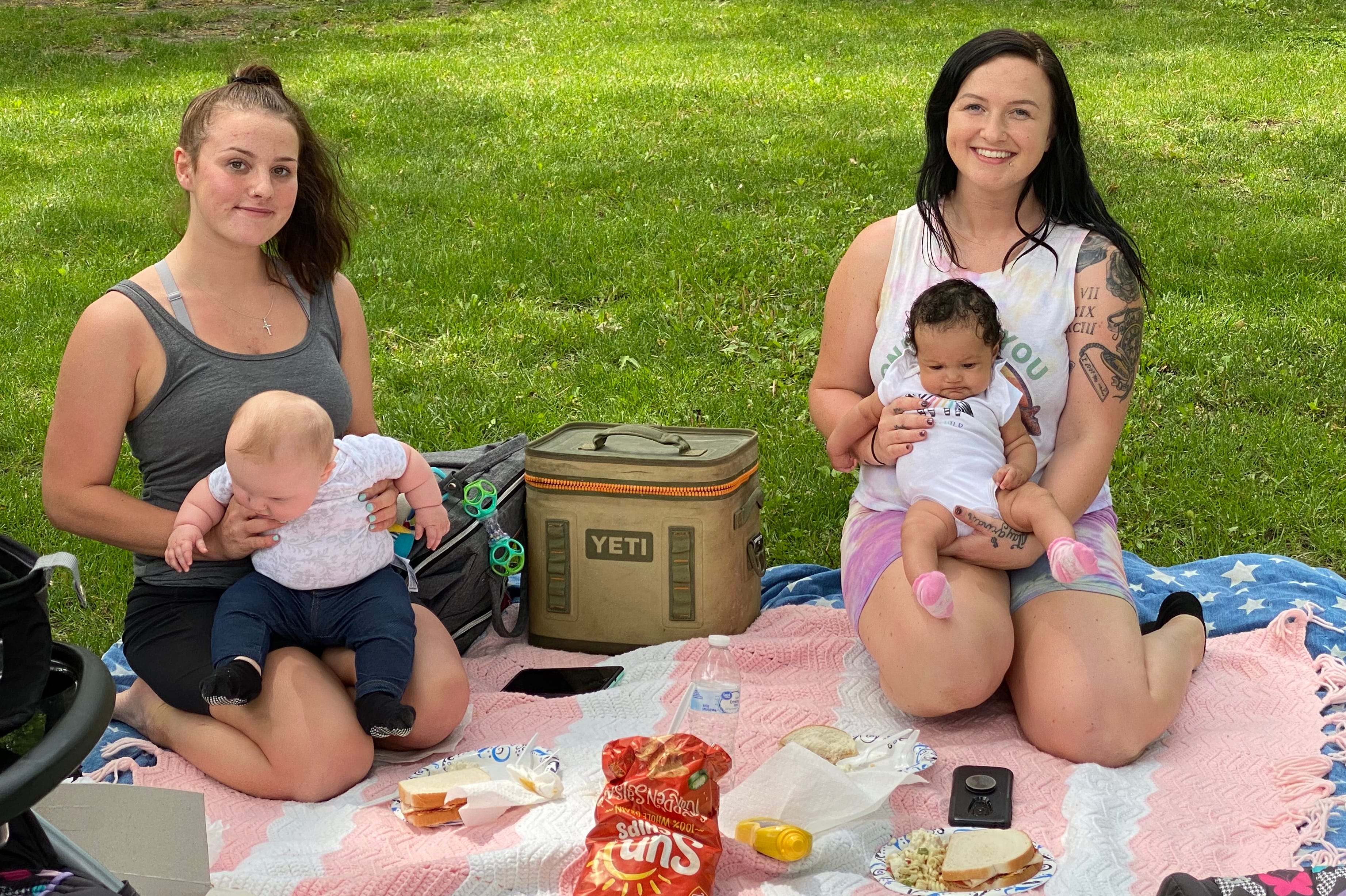 Lacey Cody, left, holds her 6-month-old daughter while picnicking at David Shepherd Park in Oak Park, MI with her sister, Tory McClellan, who is holding her 3-month old daughter.