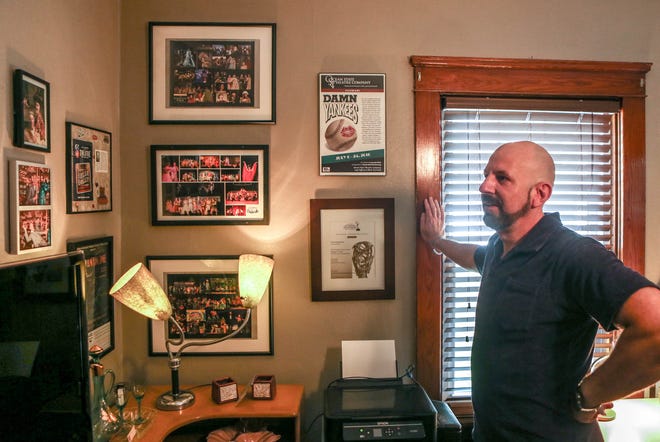 Glenn Zienowicz, a theater teacher at Nathan Bishop Middle School, talks about past works. Some of them are featured in photographs on the walls of his home office.