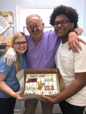 Dr. Francis Mills, center, celebrates a college sendoff moment with two young staff members, his granddaughter Caitlyn Sauls, and Noah Alexander.