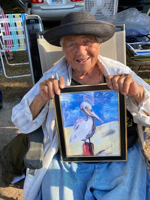 Alice Gerber shows one of her paintings at a recent Tybee Island Farmers Market. She donates what she receives to a local Parkinson's program. She signs every piece and remembers every buyer.