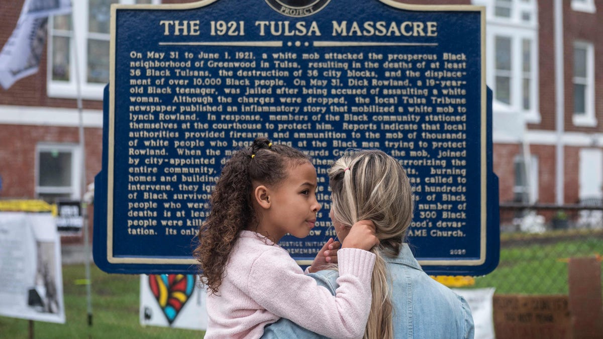 A mother holds her daughter as she reads a sign, before the arrival of US President Joe Biden, in the Greenwood district on the 100th anniversary of the 1921 Tulsa Massacre in Tulsa, Oklahoma, on June 1, 2021.  In Tulsa, the city that still bears the scars of a 1921 racial massacre, African American residents are eagerly awaiting the arrival of President Joe Biden on Tuesday, hoping he will hear their call for financial reparations.