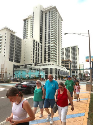 A group of tourists walk along Atlantic Avenue on Friday in front of the $192 million Protogroup twin-tower hotel-condominium project. The project's hotel, Daytona Grande, had its soft opening this week, although many of the hotel's amenities including its fitness center, pool and ocean walkway aren't yet completed.