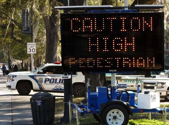 A University of Florida police officer watches traffic pass a warning sign that reads "Caution High Pedestrian Traffic Area Ahead," during a pedestrian safety operation in January.