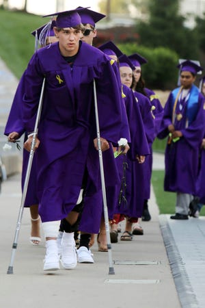 Los graduados de Burlington High School, incluido Blake Myers en muletas, se dirigen a recoger sus diplomas durante el ejercicio de graduación de la escuela, el sábado 5 de junio de 2021, en el estadio Bracewell. Myers recibió un disparo la noche anterior en las piernas mientras asistía a una fiesta.