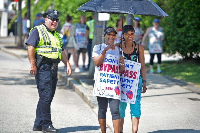 Nurses Kilsi Espinosa and Lamoy Toban share a laugh with a police officer as they walk the picket line in June.
