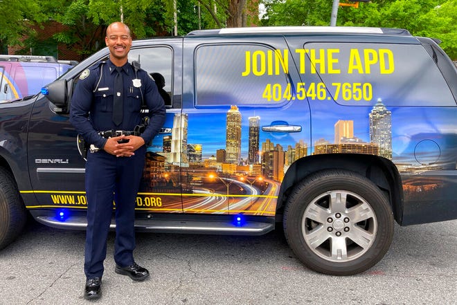 In this May 5, 2021, photo Atlanta Police Officer Philip Darrett poses for a photo in front of the SUV he uses to help recruit new officers, in Atlanta. Darrett has been tapped to serve as "Your Favorite Recruiter," appearing in videos that are streamed live on social media. He pops up at locations around Atlanta urging people to come out and chat with him about policing. (AP Photo/Kate Brumback)