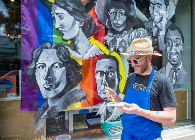 Local artist and educator Ben Koch paints a mural on the window at Beausoleil Books & Whisper Room Tuesday. Every author depicted in the mural is or was an openly gay activist.