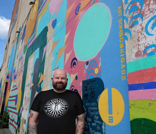 Dan Coffield, a Firestone High School art teacher and community artist involved with youth programs, stands Tuesday in front of a mural that he helped to coordinate on the wall of Crave Restaurant in Akron.