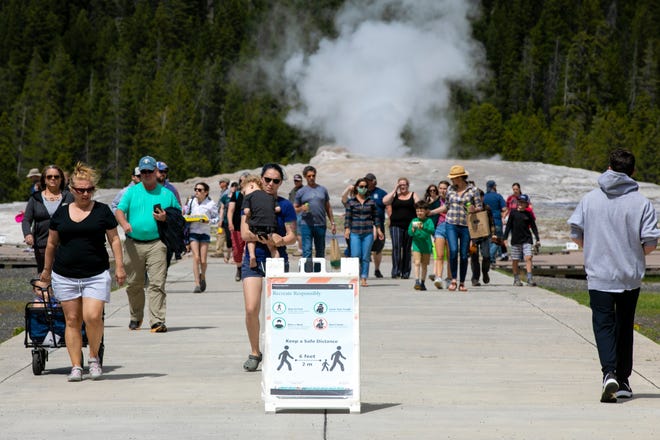 In this photo Monday, June 1, 2020, visitors walk away from Old Faithful as a sign of COVID-19 safety on a sidewalk in Yellowstone National Park in Wyoming.