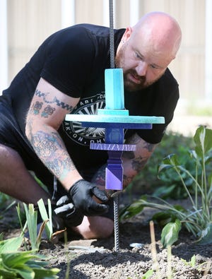Dan Coffield checks the level of a student artwork totem pole Thursday in the courtyard of the University of Akron's Schrank Hall.