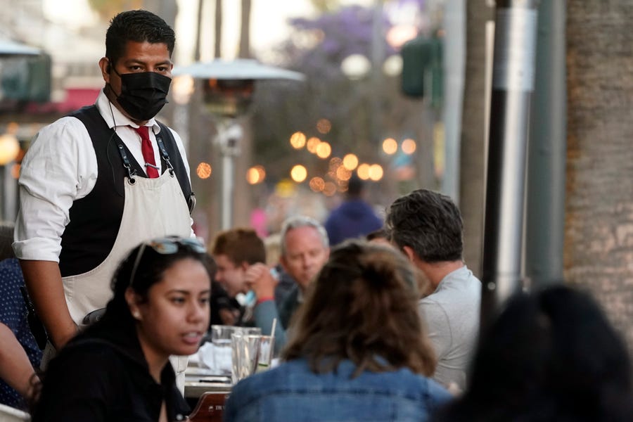 In this June 9, 2021, file photo, a server tends to customers in an outdoor dining area amid the COVID-19 pandemic on The Promenade, in Santa Monica, Calif. California regulators on Thursday approved revised worksite pandemic rules that allow fully vaccinated employees the same freedoms as when they are off the job.