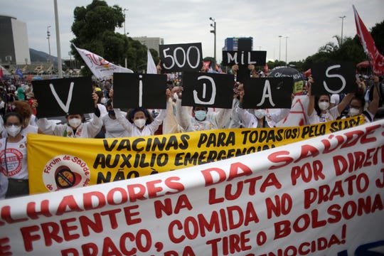 Women simultaneously hold up placards with a message that reads in Portuguese; "500K deaths! His fault!" during a demonstration against Brazilian President Jair Bolsonaro's handling of the coronavirus pandemic and economic policies protesters say harm the interests of the poor and working class, in Rio de Janeiro, Brazil, Saturday, June 19, 2021.