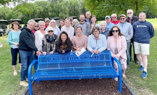 Odine Smulan's kids and grandkids, Kiwanis members and others gather around the new bench at Minakwa Golf Course.