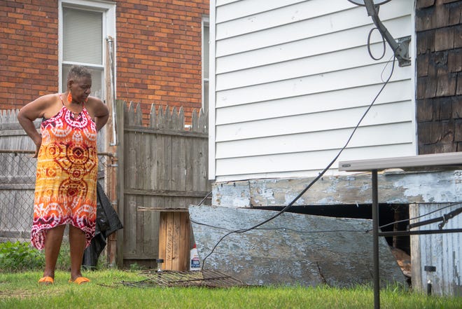 Detroit resident Daisy Jackson examining an opening in the back of her home that is usually propped closed using different crates to keep rodents from crawling underneath her home.