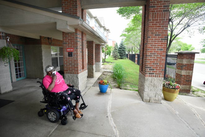 Beatrice Segur, 75, in her power wheelchair, waits to get picked up by paratransit services for a physical therapy appointment in front of her home in Detroit on June 28, 2021.